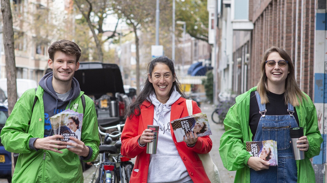 Drie vrijwilligers kijken lachend in de camera tijdens een flyeractie