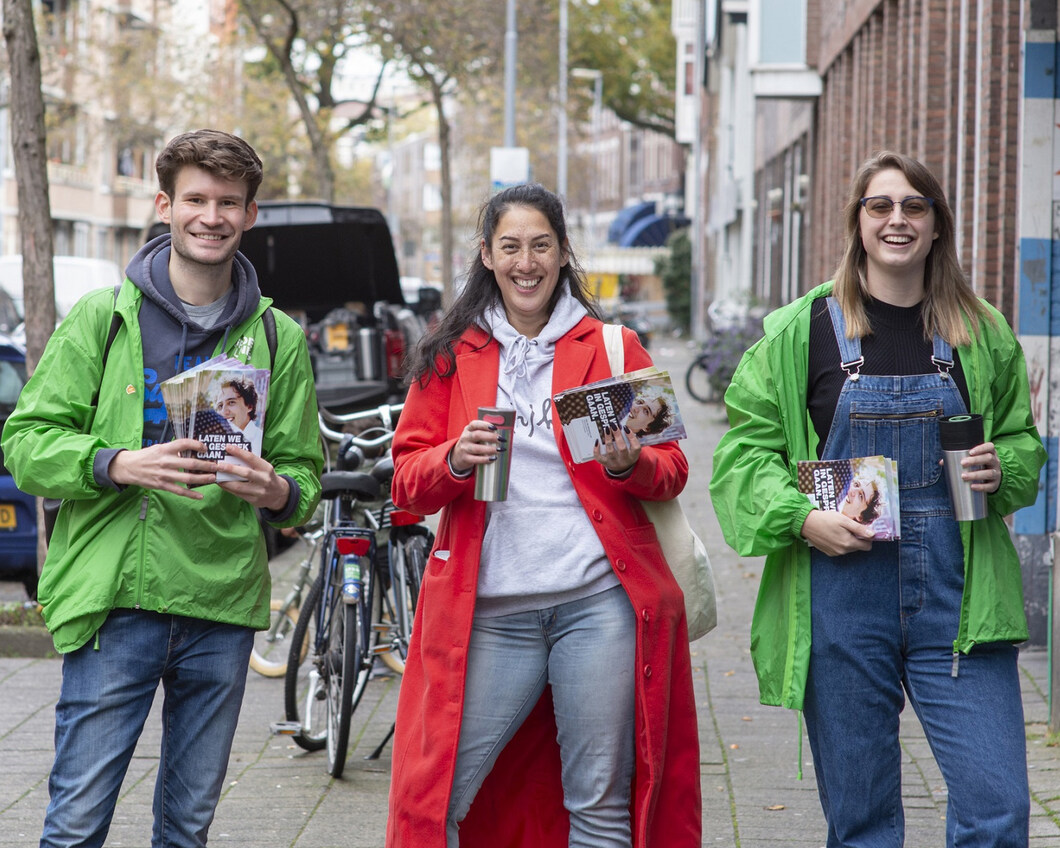 Drie vrijwilligers kijken lachend in de camera tijdens een flyeractie